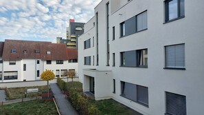 A modern residential building with multiple balconies, a paved pathway, and a small garden area with trees.