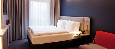 Una habitación de hotel con cama, mesita de noche y una silla roja.
