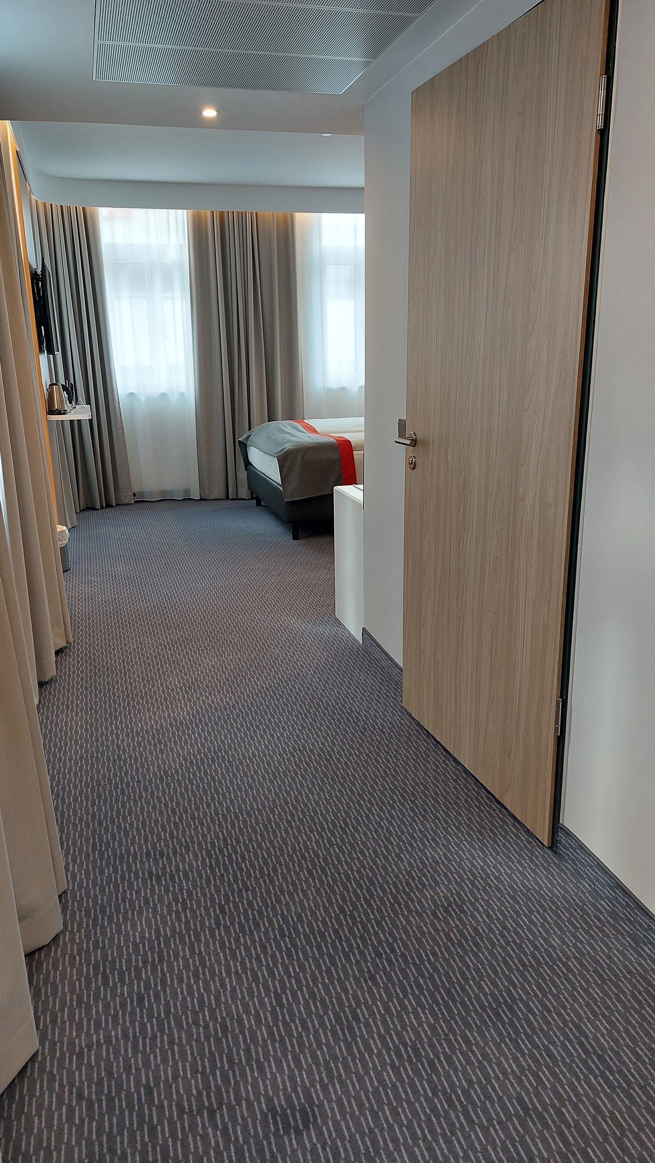 A hotel room with a large bed, a bedside table, a wardrobe, and a carpeted floor.