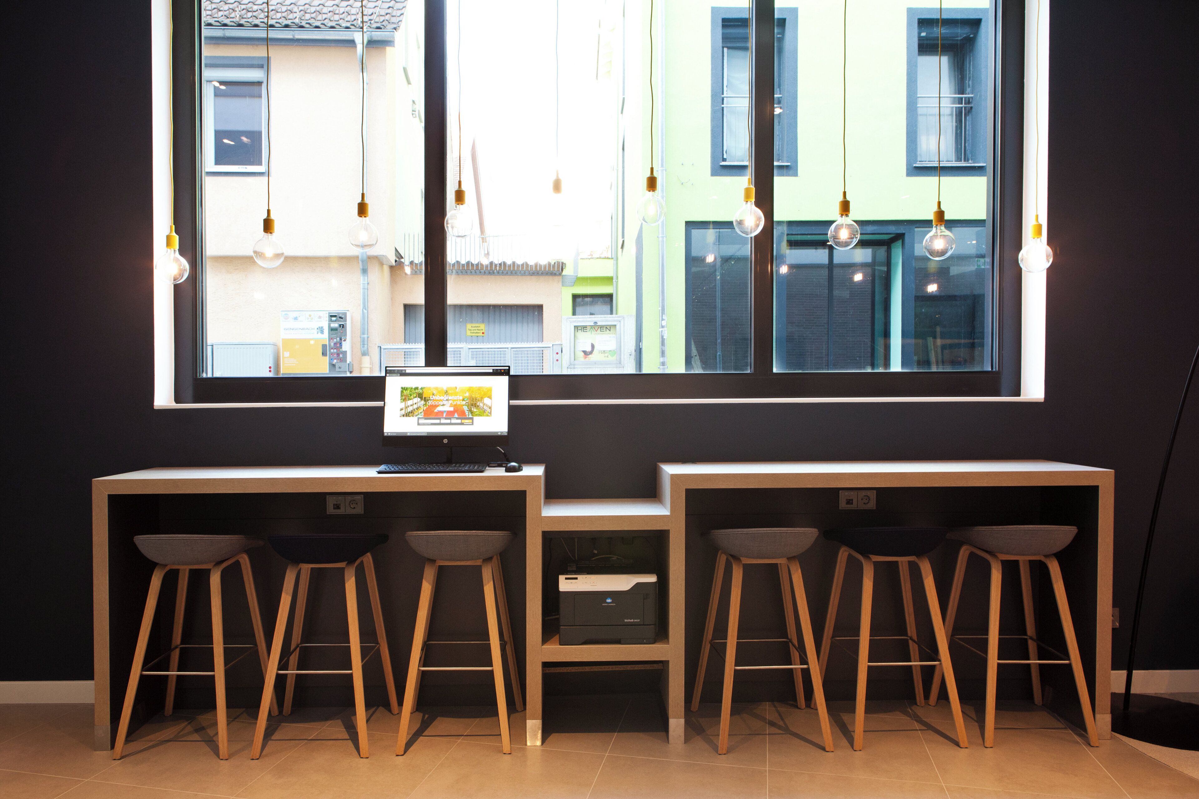 A modern workspace with a large window, two desks, and four stools.