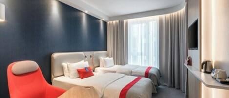 A hotel room with two beds, a red armchair, a small table, and a TV on a stand.
