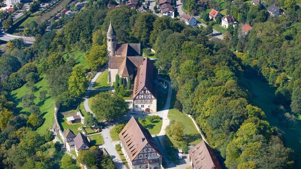 An aerial view of a historic town with a prominent church, traditional buildings, and a river.