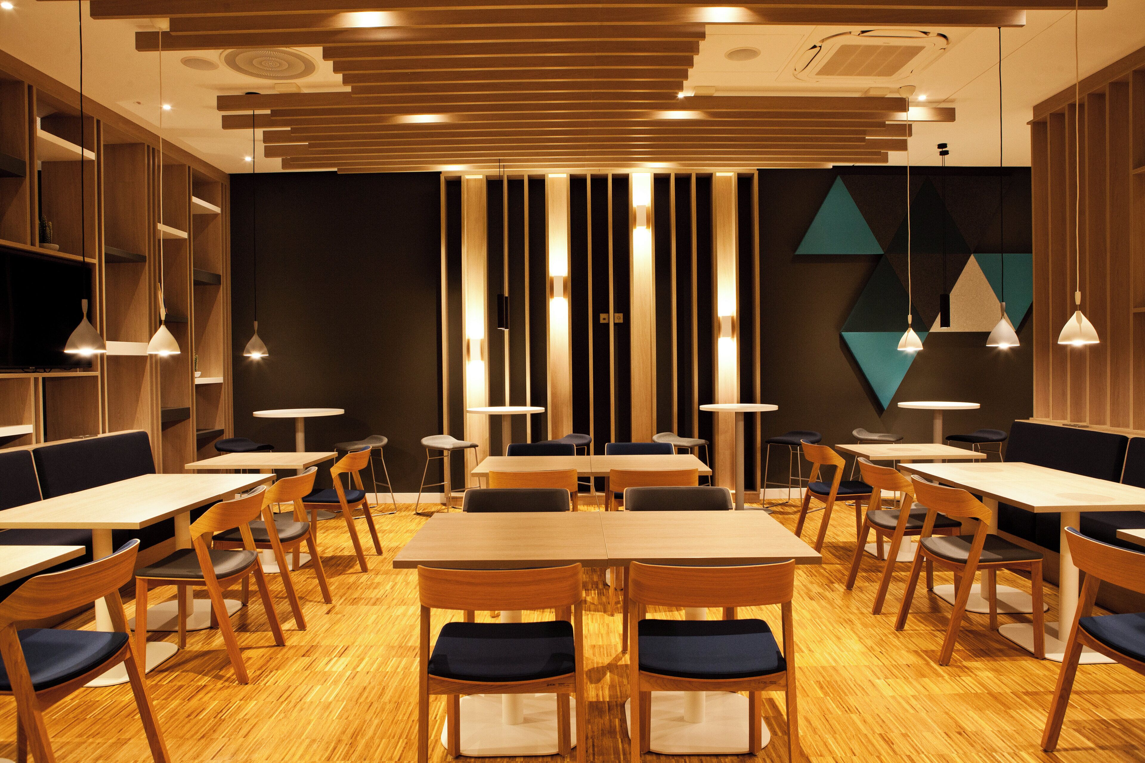 A modern restaurant interior with wooden tables and chairs, pendant lighting, and geometric wall decorations.