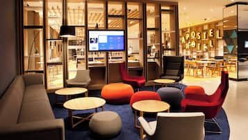Un moderno vestíbulo de hotel con áreas de estar, una recepción y una televisión mostrando la página de bienvenida del hotel.