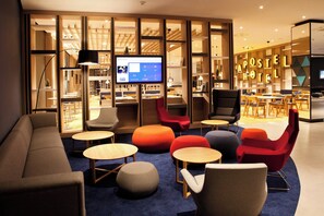 A modern hotel lobby with seating areas, a reception desk, and a television displaying the hotel's welcome page. - Holiday Inn Express Göppingen by IHG (Goeppingen)