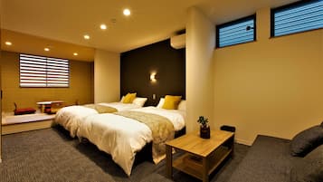 Ett modernt hotellrum med två sängar, ett litet bord, en soffa och ett stort fönster med persienner.