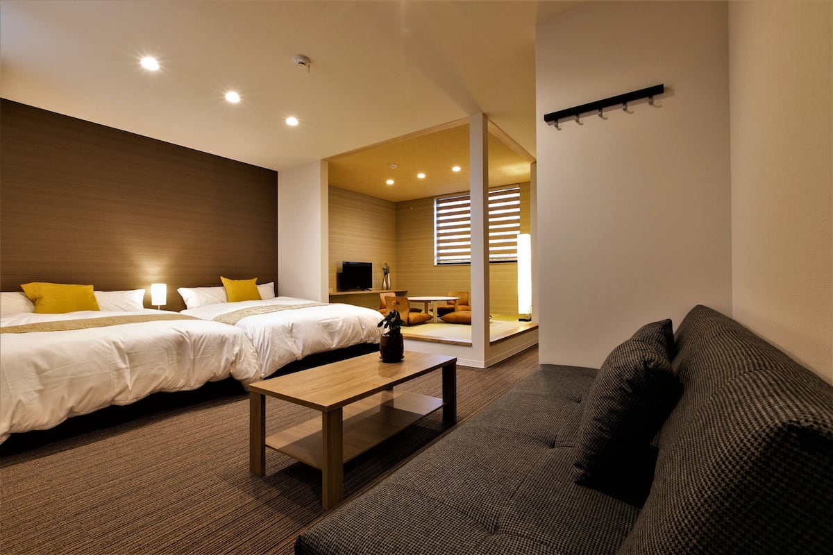 Habitación de hotel con dos camas, un sofá, una mesa de madera y un televisor.