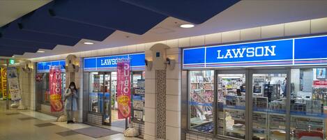 Una tienda de conveniencia Lawson con un letrero azul, ventanas de exhibición de vidrio y lonas publicitarias.
