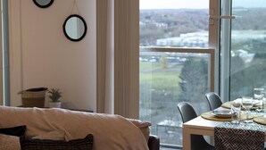 Un comedor con una mesa dispuesta para cuatro, una ventana con vistas a un paisaje urbano y dos espejos colgados en la pared.