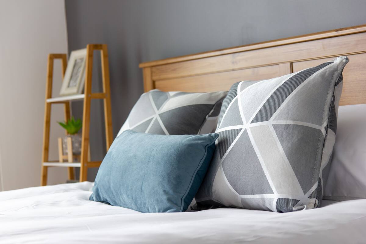 A bed with a wooden headboard, two pillows, and a small wooden ladder with a framed picture and a plant.
