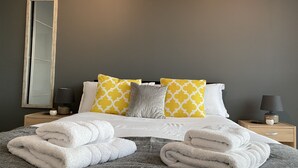 Una cama bien hecha con toallas blancas y grises, un espejo y platos decorativos en la pared.