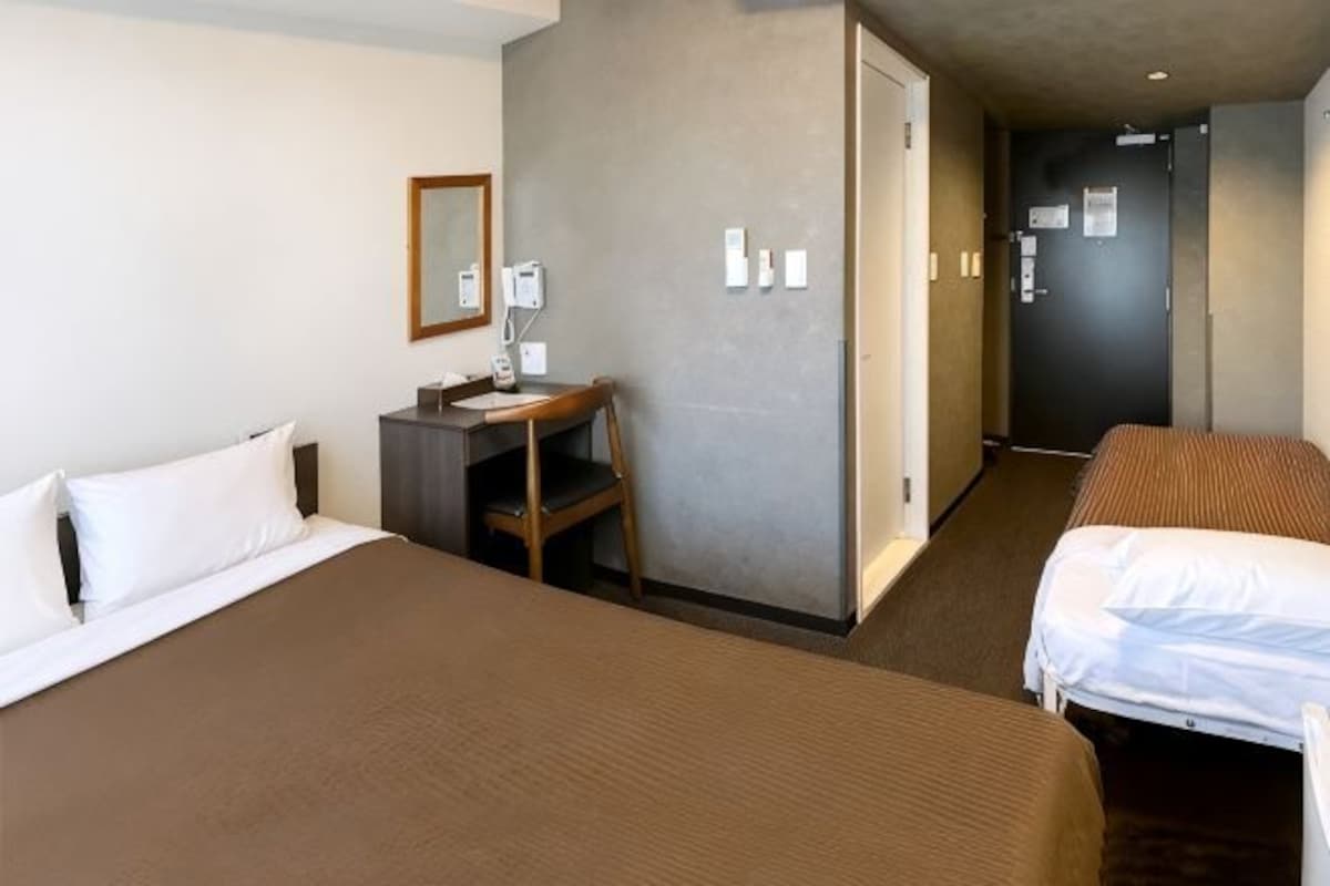 A hotel room with a large bed, a desk, a chair, and a door leading to another room.