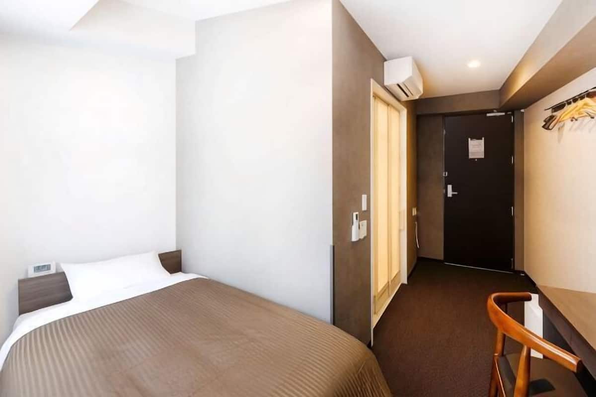 Ett hotellrum med en säng, ett skrivbord, en stol, en dörr och en luftkonditioneringsanläggning.