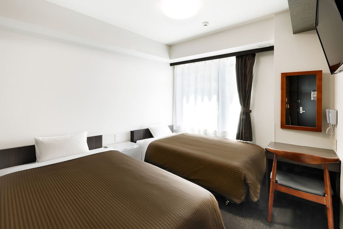 Een hotelkamer met twee bedden, een bureau, een stoel, een televisie en een raam met gordijnen.