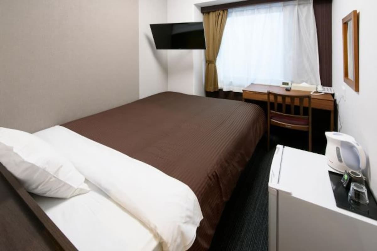 A hotel room with a bed, a desk, a chair, a television, and a coffee maker.