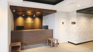Ein Hotelrezeptionstresen mit Holzoptik, einem Flachbildfernseher und einer kleinen Holzbank.
