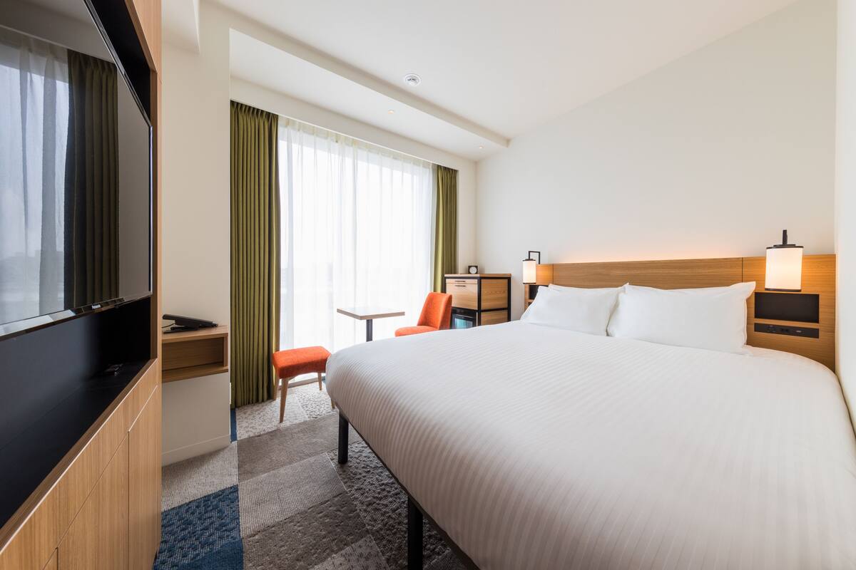A hotel room with a large bed, a TV, a desk, and a chair.