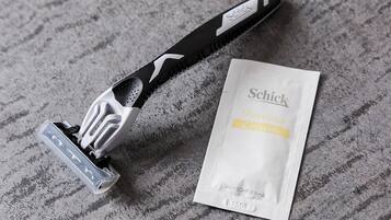 Una maquinilla de afeitar Schick y un envase de crema de afeitar sobre una superficie con textura.