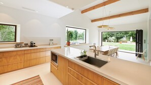A modern kitchen with wooden cabinets, a large island with a sink, and a dining area with a table and chairs. - For rent in Drôme Provençale, an exceptional property (Grignan)