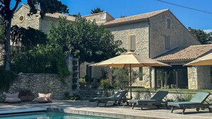 A stone building with a swimming pool, outdoor seating, and a dog visible through a window. - For rent in Drôme Provençale, an exceptional property (Grignan)