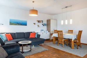 A modern living room with a sofa, a dining table with chairs, a small round table, and a hanging light fixture.