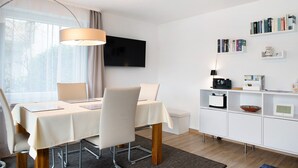 A modern dining area with a table, chairs, a TV, bookshelves, and a clock. - Apartment 'Fewo Gartenterrasse' with Private Terrace, Garden, and Wi-Fi (Meersburg)