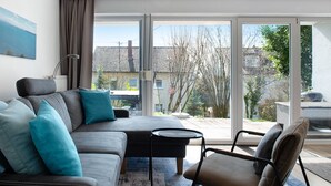 A modern living room with a sofa, armchairs, a small round table, and a view through large glass doors. - Apartment 'Fewo Gartenterrasse' with Private Terrace, Garden, and Wi-Fi (Meersburg)