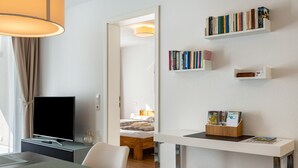 Une chambre d’hôtel moderne équipée d’un téléviseur à écran plat, d’un bureau avec un ordinateur, d’une bibliothèque et d’un lit avec une tête de lit en bois.