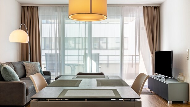 Un salon moderne comprenant une table à manger, un canapé, un téléviseur et de grandes fenêtres avec des rideaux.