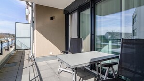 Un balcon avec une table et des chaises, une porte vitrée et une vue sur les immeubles.