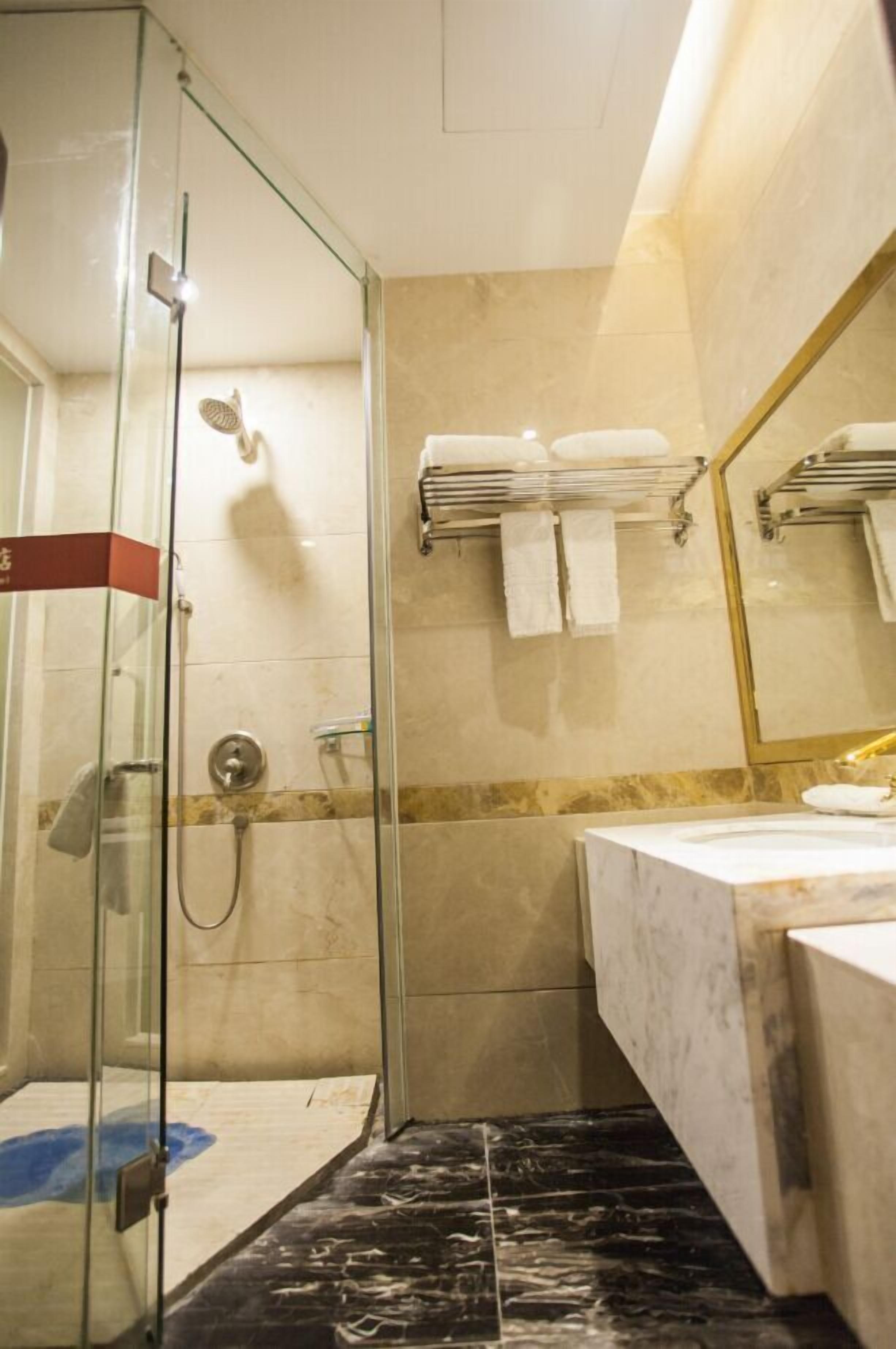 Bany d'hotel amb dutxa de vidre, terra de rajola de marbre, un lavabo i una barra de tovalloles.