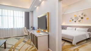 Quarto de hotel com cama, escrivaninha, cadeira, televisão e parede decorada com pratos.