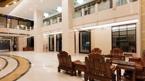 Um hall espaçoso com pé-direito alto, área de estar central com mobiliário de madeira e uma grande janela que oferece vista do interior.