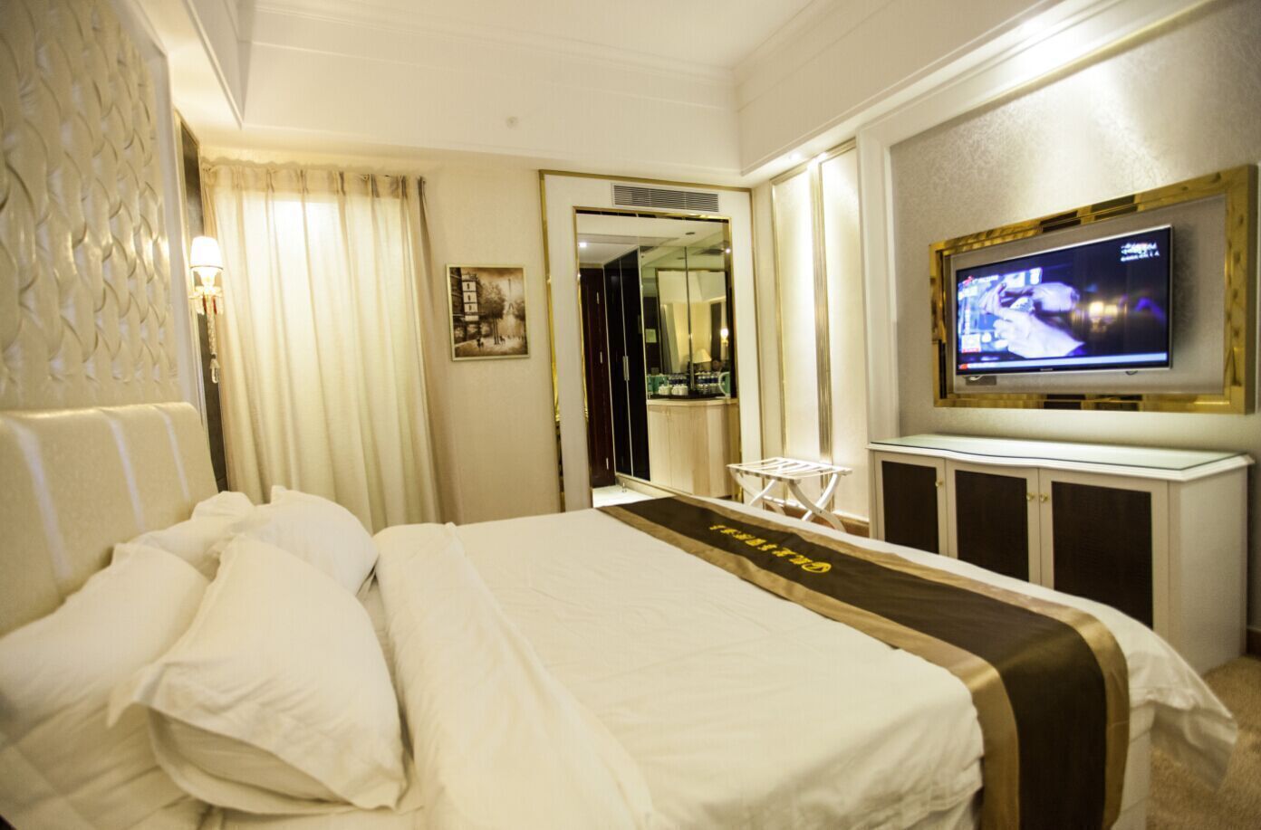 Una habitación de hotel con una cama grande, un televisor, un espejo y una mesita.