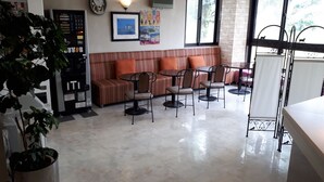 A modern lounge area with a sofa, chairs, a coffee machine, and a large window providing natural light. - Okazaki Single Hotel (Okazaki)