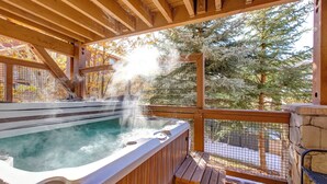 Ein Whirlpool mit aufsteigendem Dampf, umgeben von einer Holzboden-Terrasse und Steinmauern, mit Blick auf eine verschneite Landschaft.