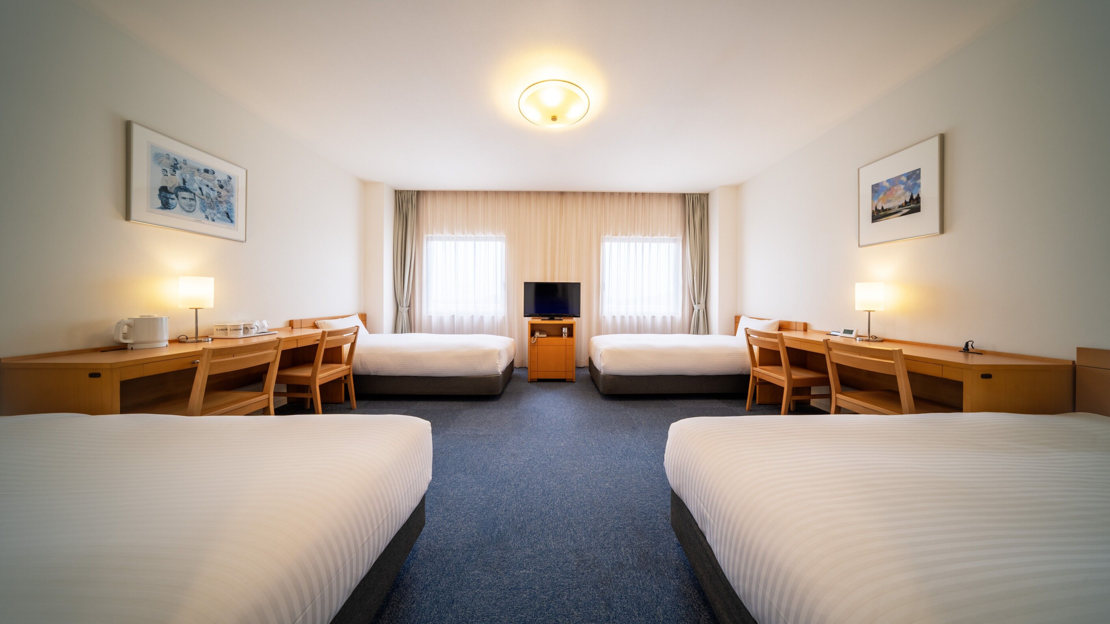 A hotel room with two beds, a desk, a chair, a television, and a coffee maker.