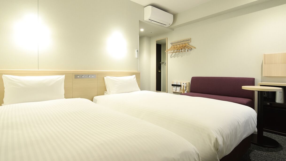Habitación de hotel con dos camas, un escritorio, una silla, un equipo de aire acondicionado y un espejo.
