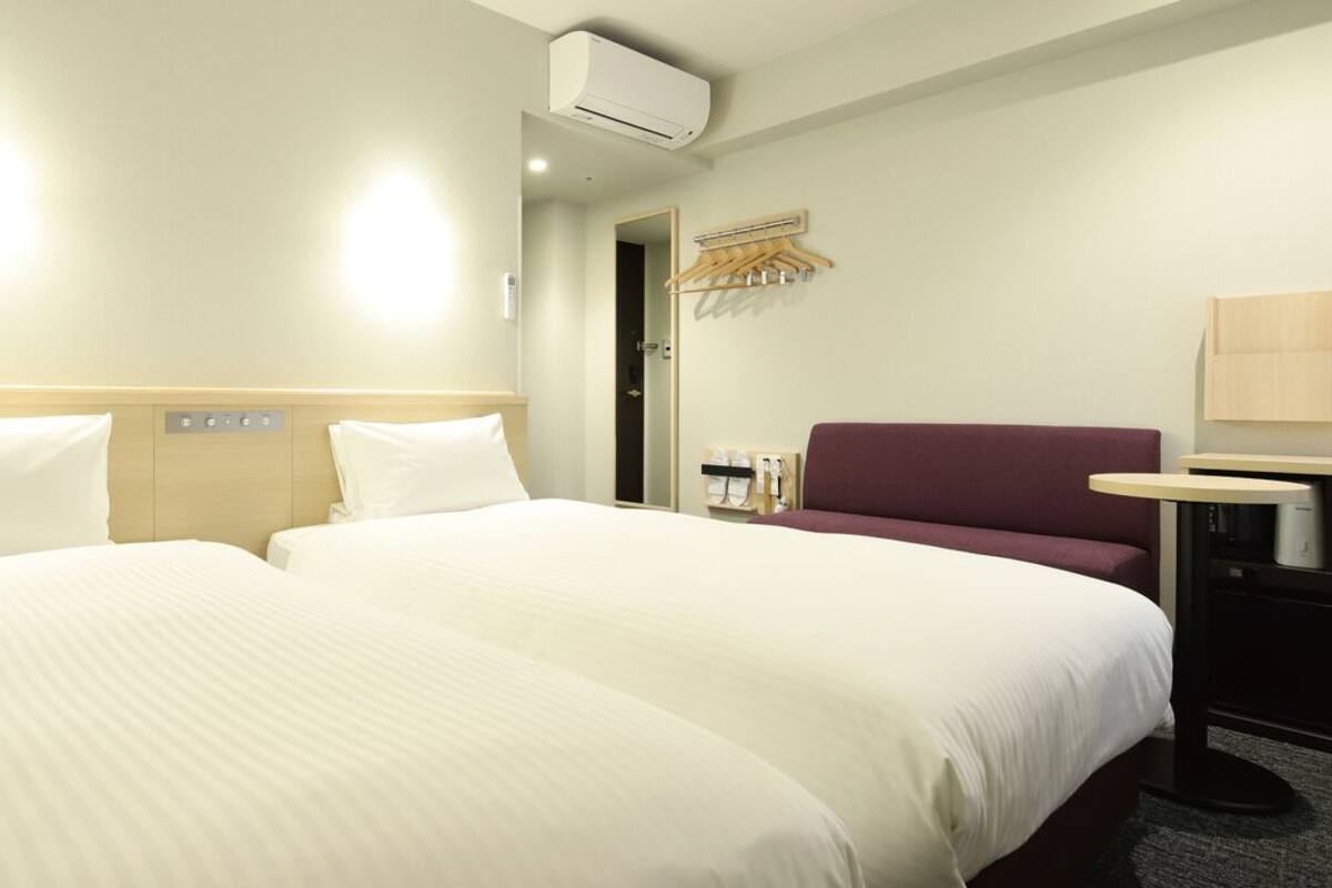 Ein Hotelzimmer mit zwei Betten, einem Schreibtisch, einem Stuhl, einer Klimaanlage und einem Spiegel.