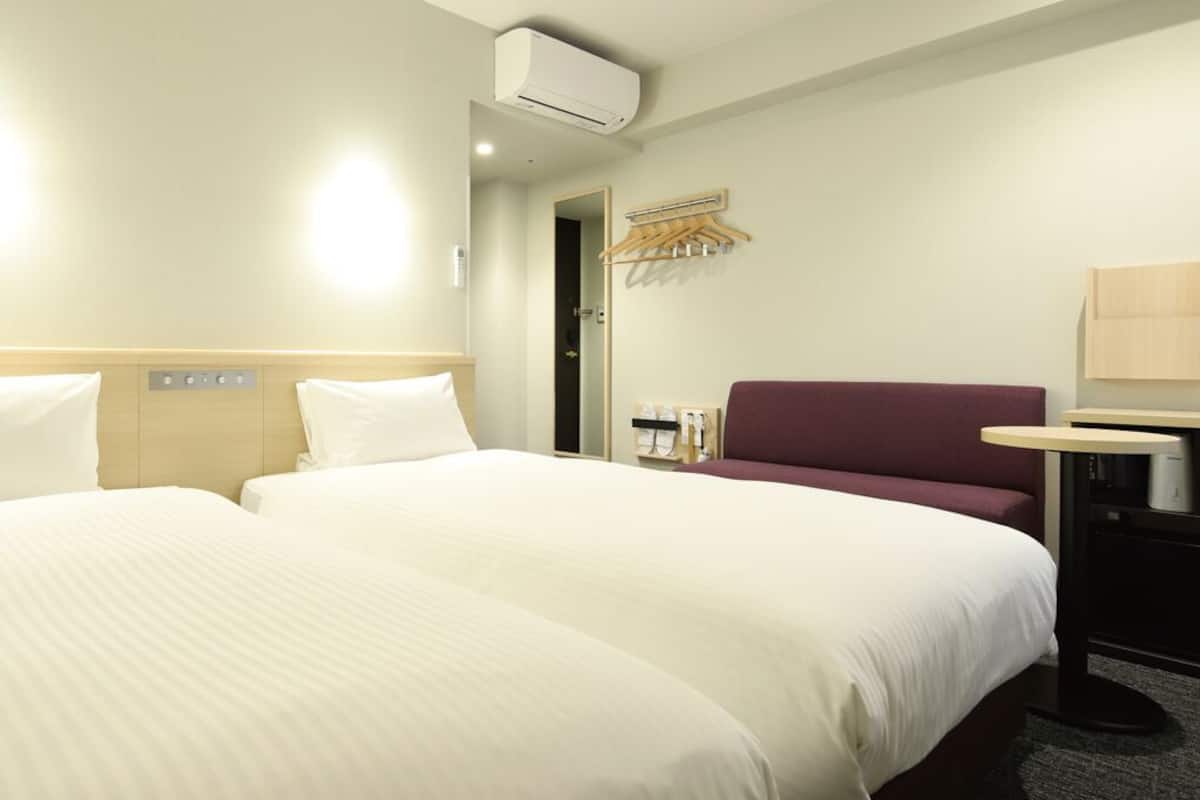 Ein Hotelzimmer mit zwei Betten, einem Schreibtisch, einem Stuhl, einer Klimaanlage und einem Spiegel.