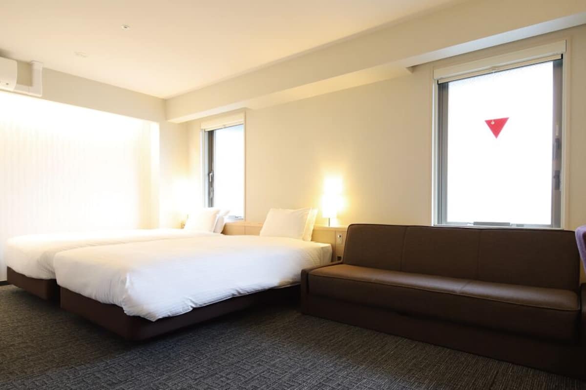 Ein Hotelzimmer mit Bett, Sofa, Schreibtisch und einem Fenster mit Jalousien.