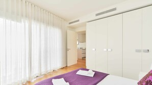 Ein Hotelzimmer mit einem Bett, einer violetten Tagesdecke, weißen Vorhängen und einem Kleiderschrank.