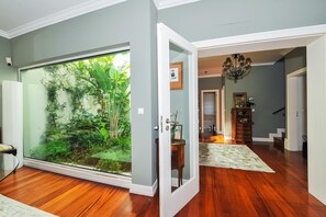 Quarto com uma grande porta de vidro deslizante que dá para um jardim exuberante, piso de madeira, um candelabro e uma escada.