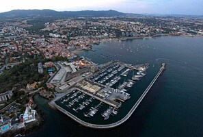 Vue aérienne d’une ville côtière, avec une marina remplie de bateaux, entourée de quartiers résidentiels et dominée par un port important.
