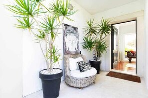 Decoração moderna com uma cadeira de vime, plantas em vasos grandes e uma estátua de Buda.