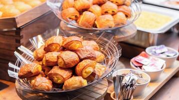 A buffet with various baked goods, including croissants and pastries, and a selection of condiments and utensils.