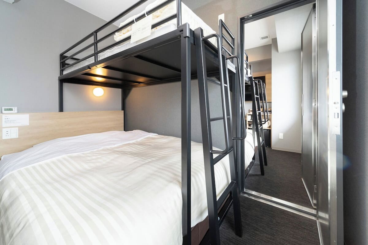 Ein Schlafraum mit Etagenbett, Holz Kopfteil, Nachttisch und einer Wanduhr.