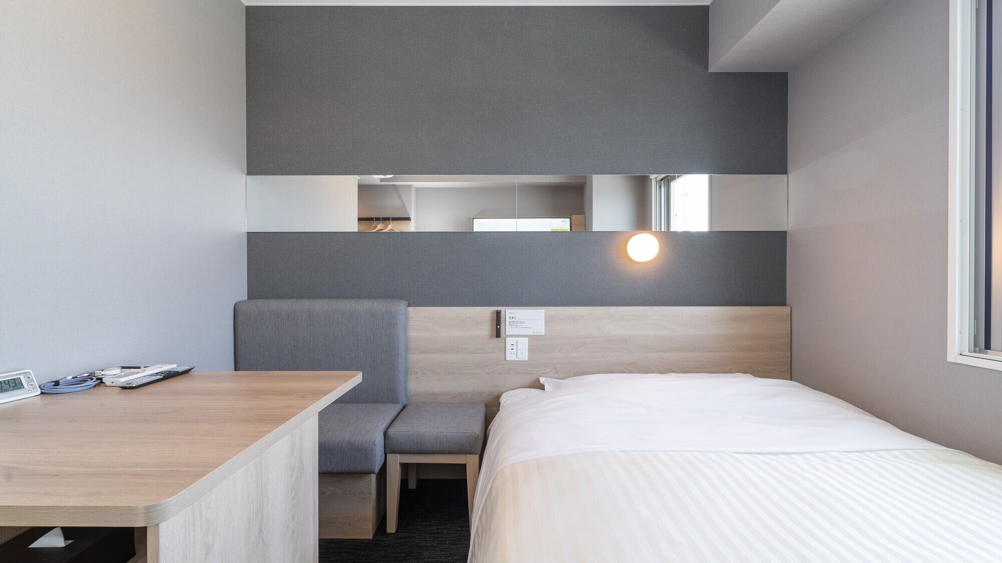 Une chambre d’hôtel moderne équipée d’un lit, d’un bureau, d’une chaise, d’un petit coin salon et d’un miroir.