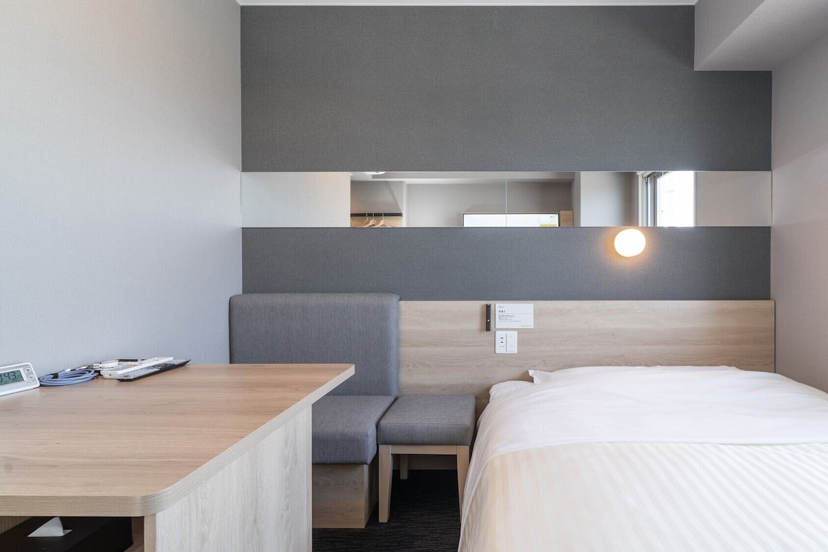 Ein modernes Hotelzimmer mit Bett, Schreibtisch, Stuhl, einer kleinen Sitzecke und einem Spiegel.
