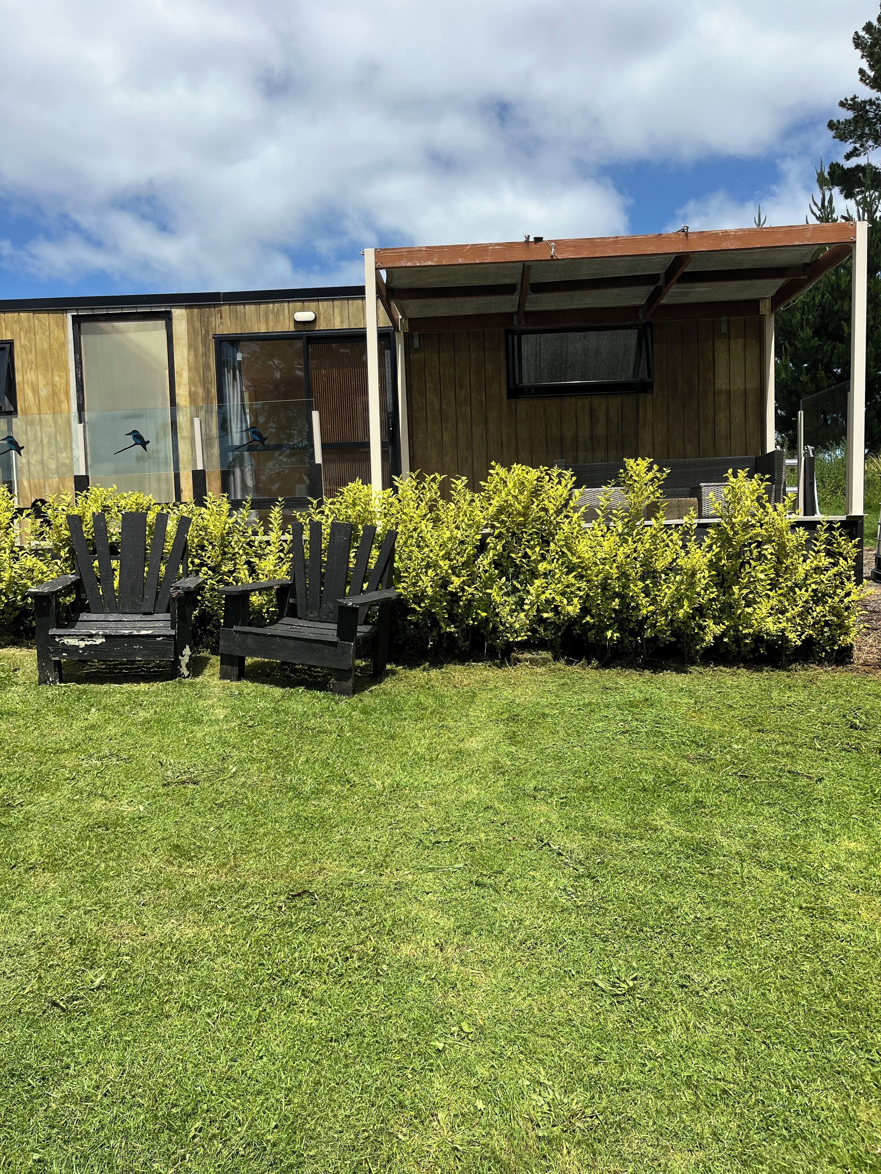 Un bâtiment moderne doté d’une façade en bois, de grandes fenêtres et d’un espace extérieur abrité avec des bancs, aménagé pour accueillir les clients.